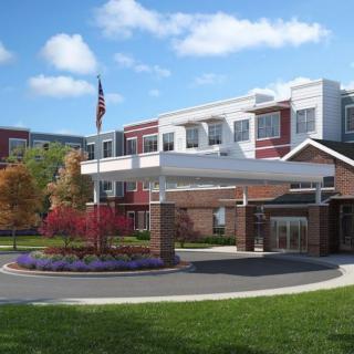 A modern hospital building with a landscaped entrance and an American flag flying under a blue sky.