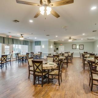 A spacious dining room with neatly arranged tables and chairs, featuring wooden flooring and ceiling fans.