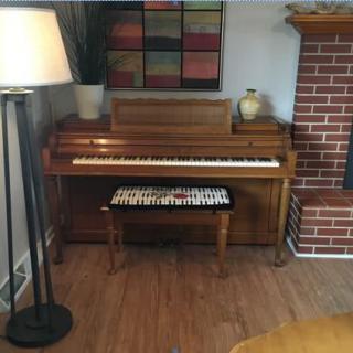 A cozy living room corner featuring a piano with a bench, a nearby floor lamp, and a brick fireplace.