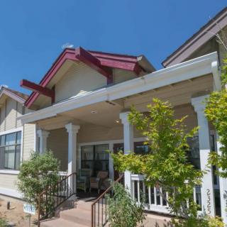 A residential house with a front porch and surrounding greenery under a clear blue sky.