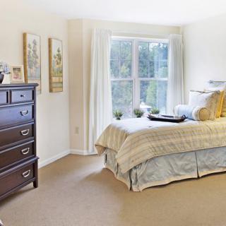 A cozy bedroom with a neatly made bed, dresser, and a large window allowing natural light to fill the space.