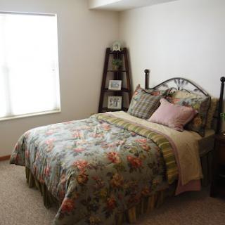 A cozy bedroom featuring a floral patterned bedspread and a shelf with decorative items.