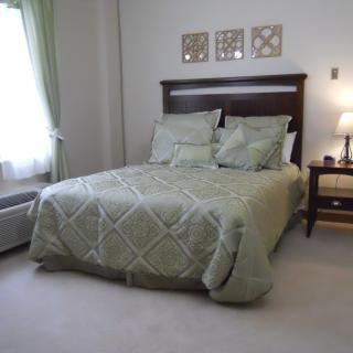 A neatly arranged bedroom with a green bedspread, bedside lamp, and wall decor.