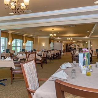An elegantly set dining area with multiple tables and chairs, featuring chandeliers and a warm ambiance.
