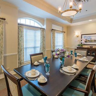 A well-decorated dining room with a long table set for a meal, featuring elegant dinnerware and a chandelier overhead.