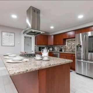 A modern kitchen featuring a large island with granite countertops, surrounded by wood cabinets and stainless steel appliances.