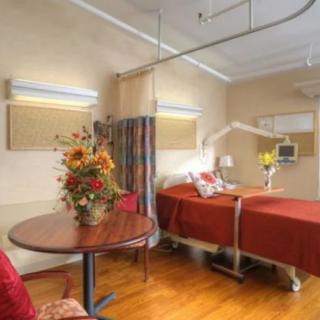 A hospital room with a bed, flowers on a table, and medical equipment.