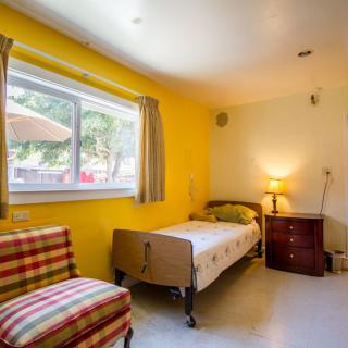 A cozy bedroom with yellow walls, featuring a single bed and a bright window.