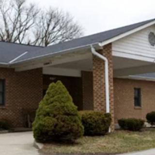 A brick building with a white roof overhang and landscaped shrubs at the entrance.