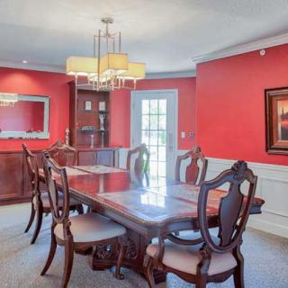 A traditional dining room with red walls, featuring a wooden table and chairs, accented by a mirror and chandelier.