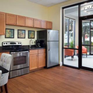 A modern kitchen with stainless steel appliances and wooden cabinetry, illuminated by natural light through large windows.