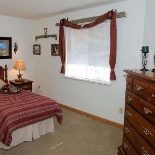 A cozy bedroom with a single bed, dresser, and window adorned with red curtains.