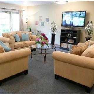 A cozy living room with beige sofas and a glass coffee table centered around a television.