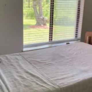 A neatly made bed by a window with a view of greenery outside.