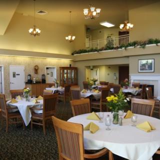 An elegant dining room with neatly arranged tables, each set with yellow napkins and floral centerpieces.