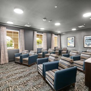 A cozy seating area with multiple chairs, carpeted flooring, and windows adorned with curtains.