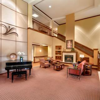 A welcoming lobby with a grand piano, comfortable seating around a fireplace, and an elegant staircase.