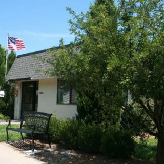 A small building with an American flag nearby, surrounded by trees and a bench in the garden.