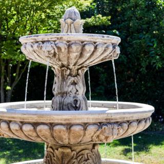 A stone fountain in a garden setting, with water cascading from the top tier.