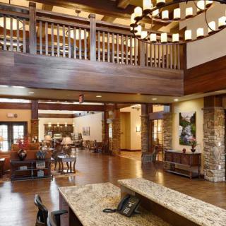 A spacious and elegantly designed lobby area featuring wooden beams, a chandelier, comfortable seating, and a reception desk.