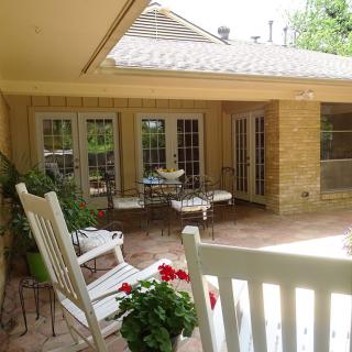 A cozy patio area with rocking chairs and outdoor seating surrounded by a brick wall and windows.
