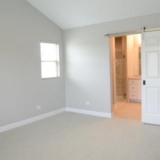 An empty room with gray walls, carpet flooring, a window, and a doorway leading to a bathroom.