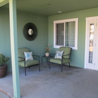 A cozy porch area with two chairs and a potted plant against a green wall.