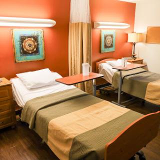 A modern hospital room featuring two beds, equipped with warm lighting and colorful artwork on the walls.