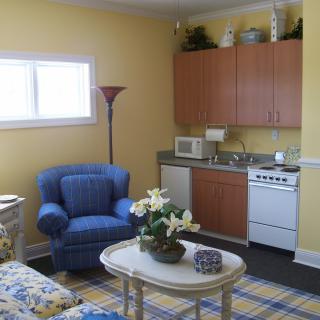 A cozy living area with a kitchenette, featuring an armchair, coffee table, and yellow walls.