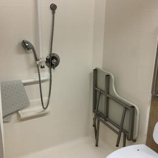 An accessible bathroom with a handheld shower head, grab bar, and foldable seat.