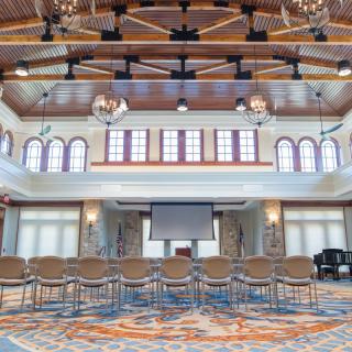 A spacious conference room with arranged seating, a projector screen, and ornate chandeliers.
