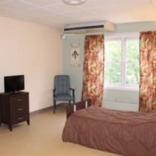 A simple bedroom with a single bed, a small TV on a dresser, and floral curtains covering the window.