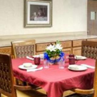 A neatly set dining table with a red tablecloth and flower centerpiece.