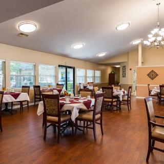 A well-lit dining room with tables set for service, featuring elegant decor and wooden flooring.