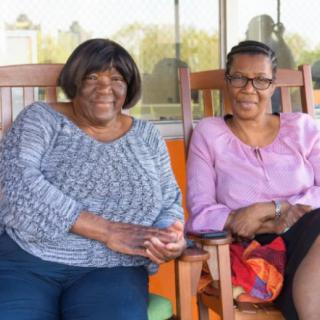 Two women sitting on chairs outdoors, smiling and enjoying a relaxed moment.