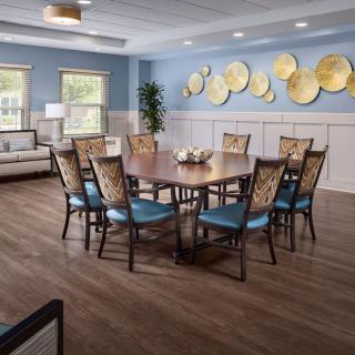 A well-decorated dining room with a large wooden table, cushioned chairs, and wall art in a bright, inviting space.
