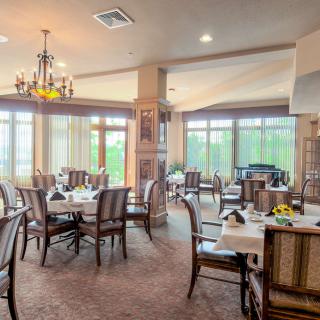 A cozy restaurant dining area with tables and chairs, featuring large windows and a chandelier.