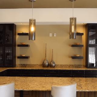 A modern kitchen interior with pendant lights, granite countertops, and decorative shelving.