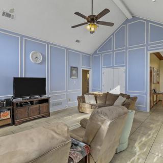 A cozy living room with blue paneled walls, featuring a sofa set, television, ceiling fan, and wooden flooring.