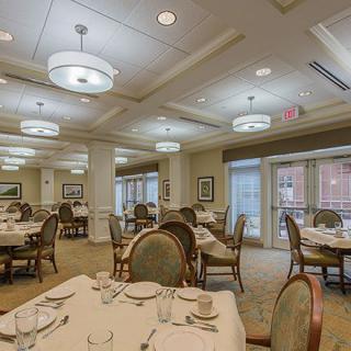 An elegant dining room with neatly arranged tables and chairs, illuminated by ceiling lights.