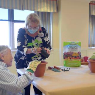 A joyful gardening session where an elderly person receives assistance in potting plants.