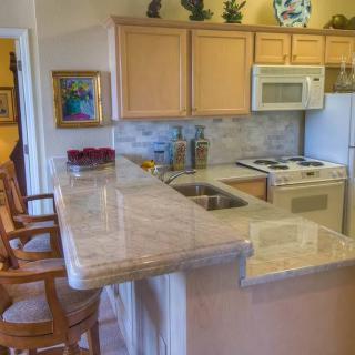 A cozy kitchen with wooden cabinets, a marble countertop, and bar stools.