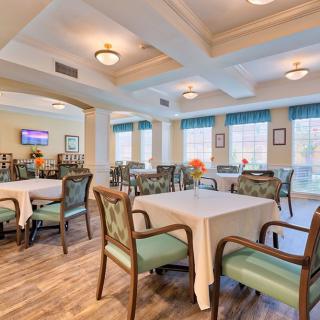 A well-lit dining room with neatly arranged tables and chairs, featuring large windows and elegant lighting fixtures.