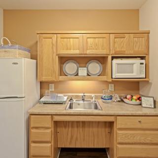 A compact kitchen setup with wooden cabinets, featuring a refrigerator, microwave, sink, and countertop with kitchenware.