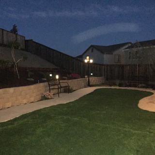 A well-lit backyard at night with artificial grass and a surrounding fence.