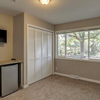 A cozy room with a large window, carpet flooring, a closet, wall-mounted TV, and a mini fridge.