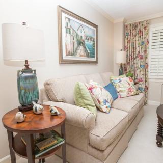 A cozy living room with a beige sofa adorned with colorful cushions, a side table with a lamp, and decorative elements.