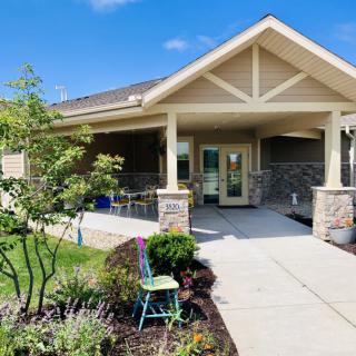 A charming residential house with a covered porch and landscaped garden, set under a clear blue sky.