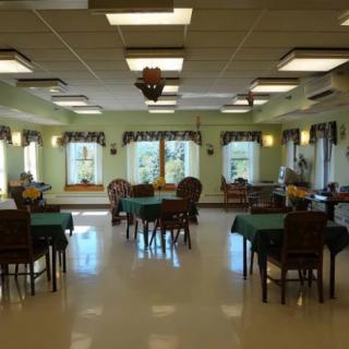 An empty dining area with tables and chairs arranged neatly, surrounded by green walls and decorated windows.