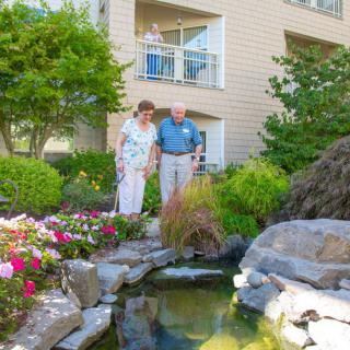 A senior couple enjoying the view of a garden with a pond outside their residential building.
